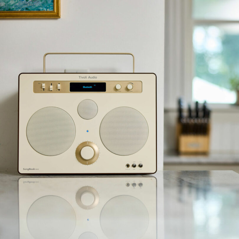 A beige Tivoli Audio Bluetooth speaker, perfect for modern gifts, with dual speakers and control knobs sits gracefully on a marble kitchen countertop.