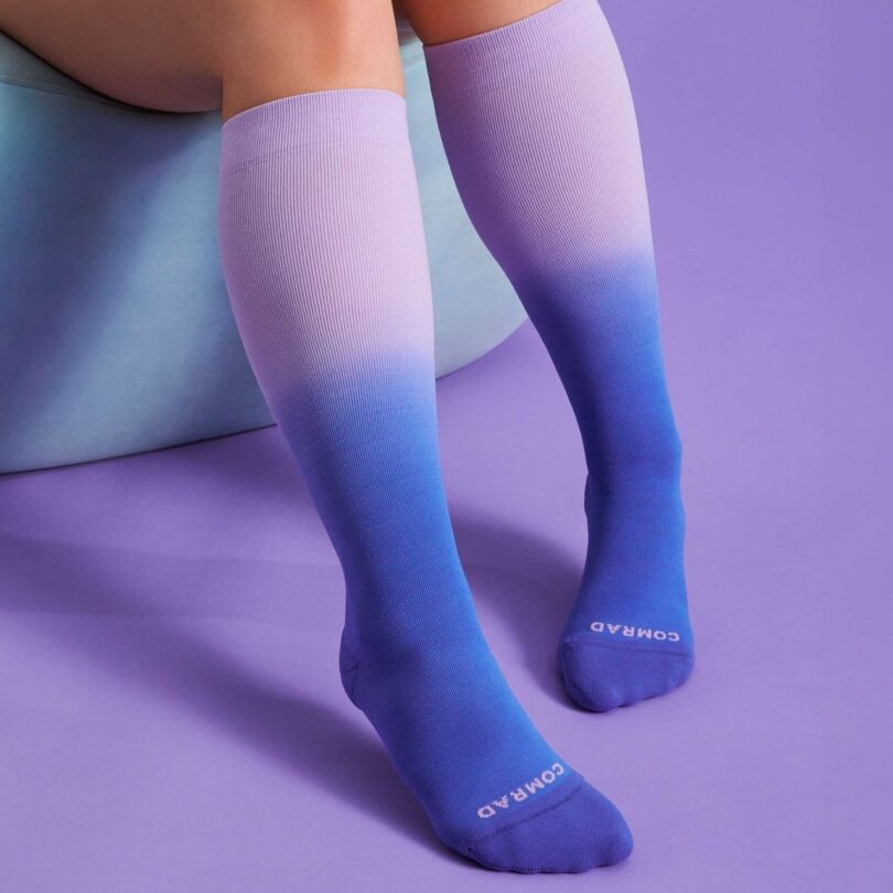 Person wearing knee-high gradient socks transitioning from light purple to dark blue, sitting on a purple surface