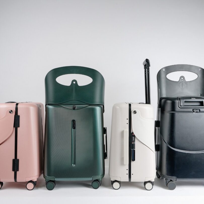 Four wheeled suitcases stand in a row; colors are pink, green, white, and black