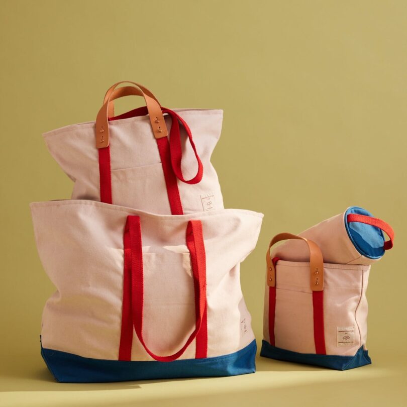 Three canvas bags with red handles and blue bottoms against a beige background