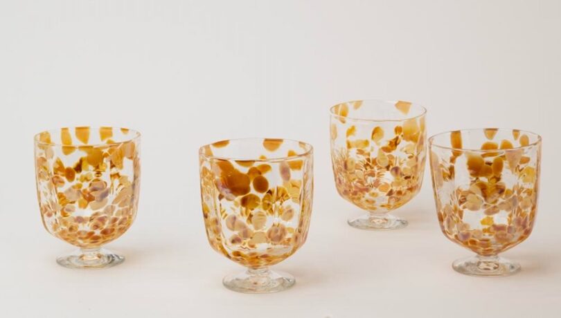 Four clear glass goblets with amber-colored speckles are arranged on a plain background