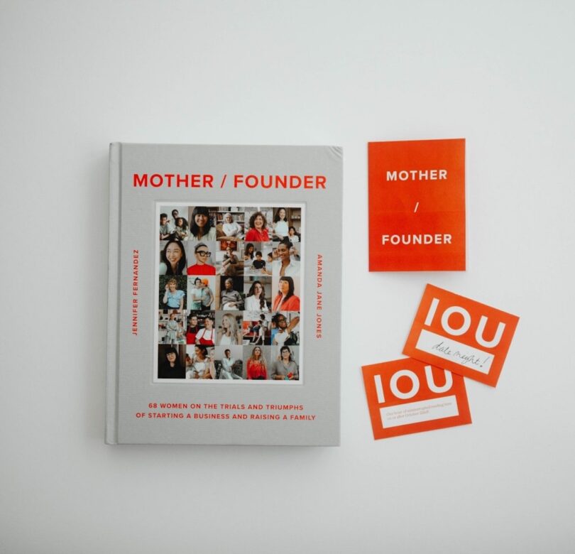 A book titled "Mother / Founder" alongside red cards with "IOU" and "Mother / Founder" on them, against a white background