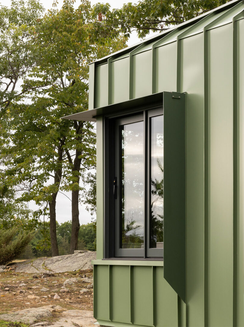 Green metal-clad building with a modern window and trees in the background.