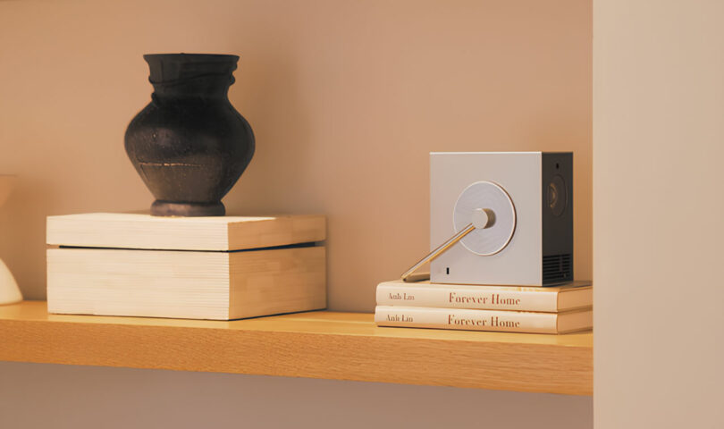 A minimalist shelf features decorative elements such as a black vase, wooden boxes, and a stack of books titled "Forever Home," all beside an LG cube-shaped object with a circular center.