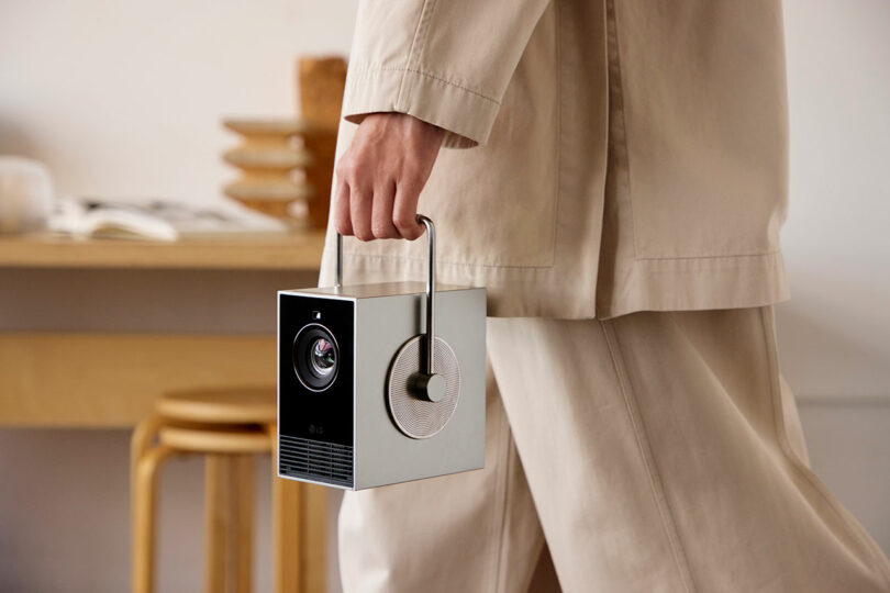 An individual confidently grasps an LG portable projector by its handle in a sleek, minimalist room.