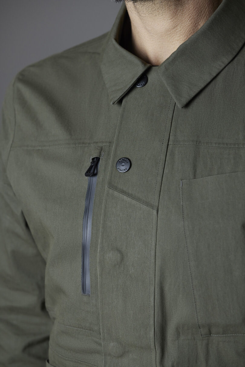 Close-up of a person wearing a dark green jacket with a button and zipper detail on the front.