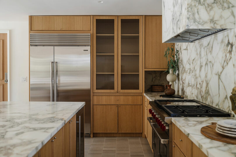 A modern kitchen with wooden cabinets, marble countertops, and a stainless steel refrigerator creates a sleek space for culinary adventures.