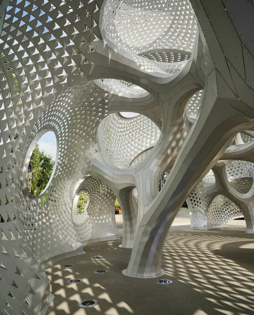 Intricate architectural structure with geometric patterns and circular openings, casting shadows on the ground.