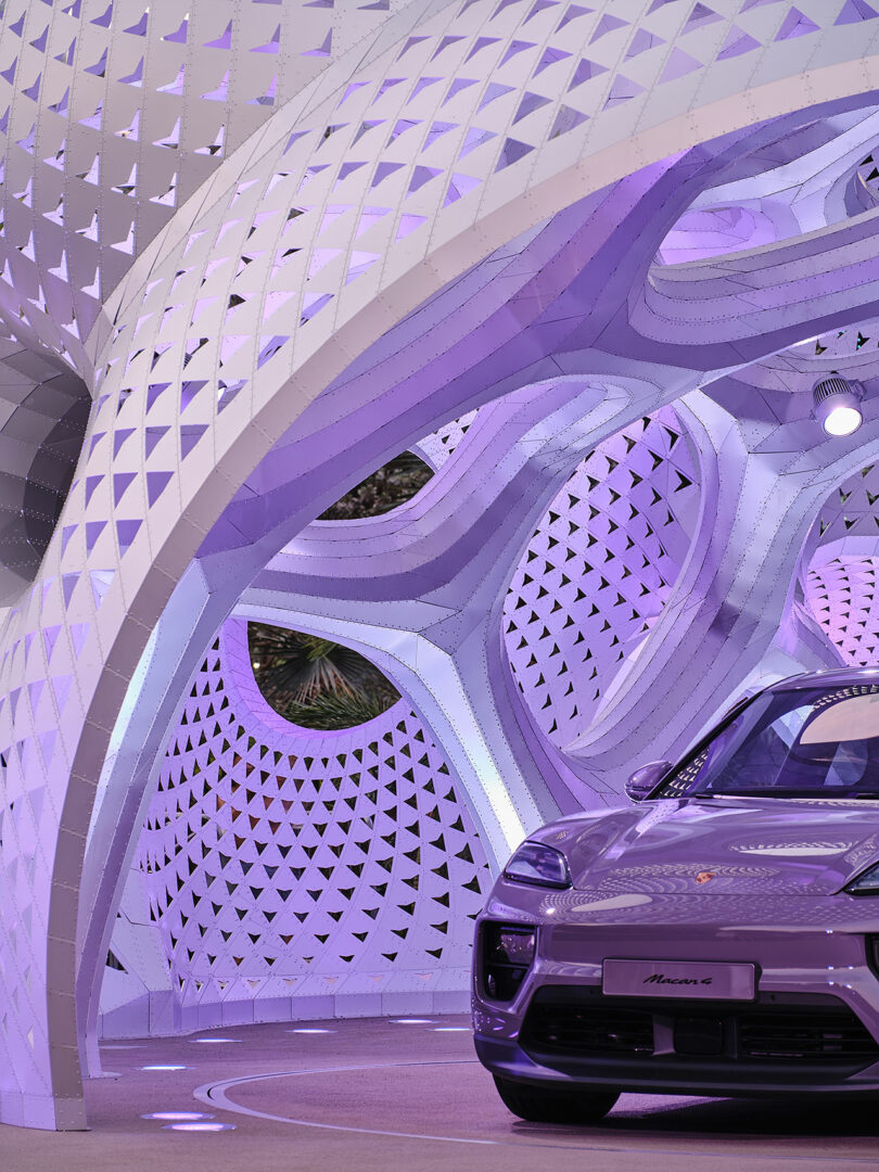 A purple car in front of a futuristic, lattice-structured pavilion with purple lighting.