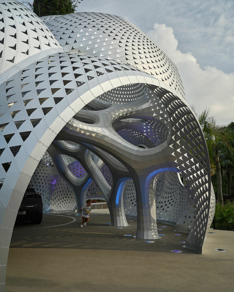 A child runs under a futuristic, metallic, dome-shaped structure with triangular perforations.