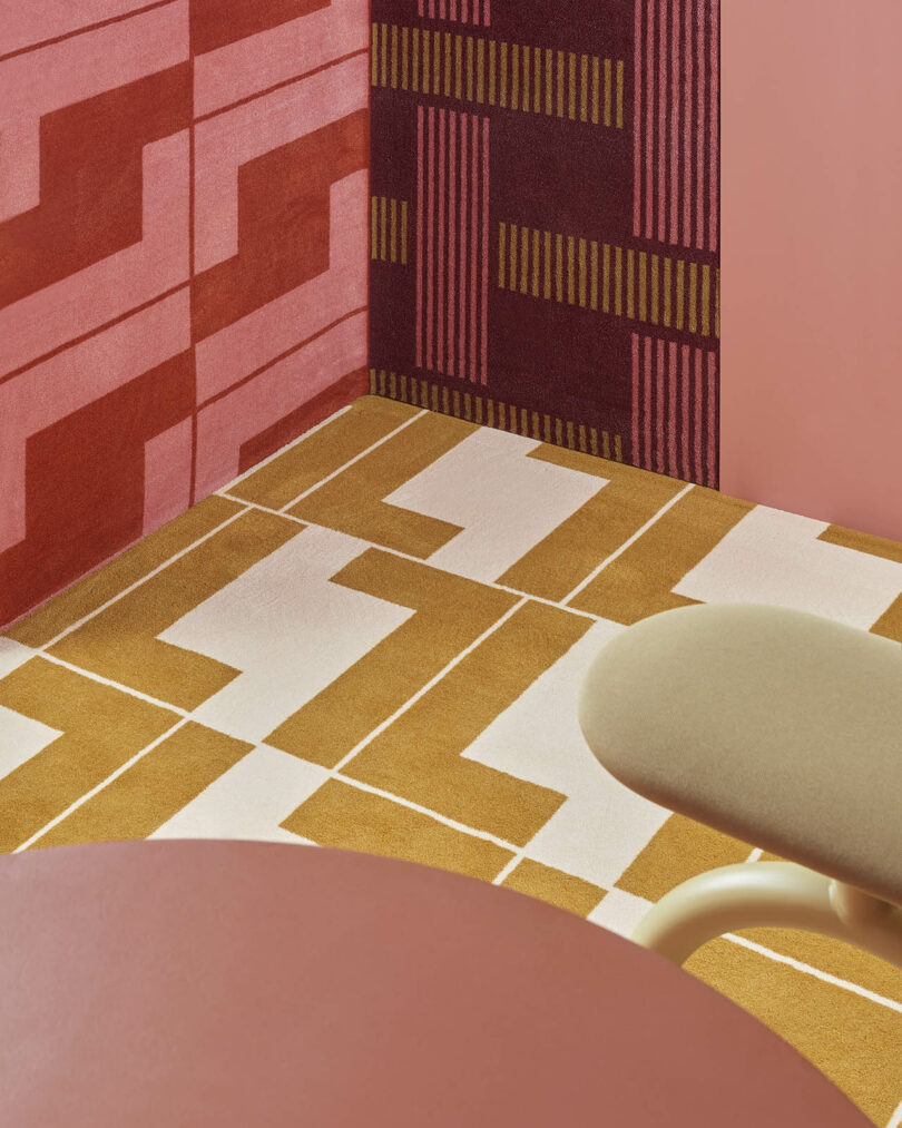 A room corner with geometric patterned walls in red and pink, and a yellow and white tiled floor. A soft beige chair and a round pink table are partially visible.