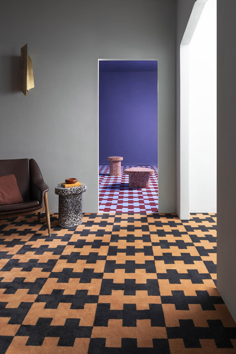 Room with a checkered floor, a brown armchair, and a marble side table. The adjacent room features a purple wall and checkered flooring with two round stools.