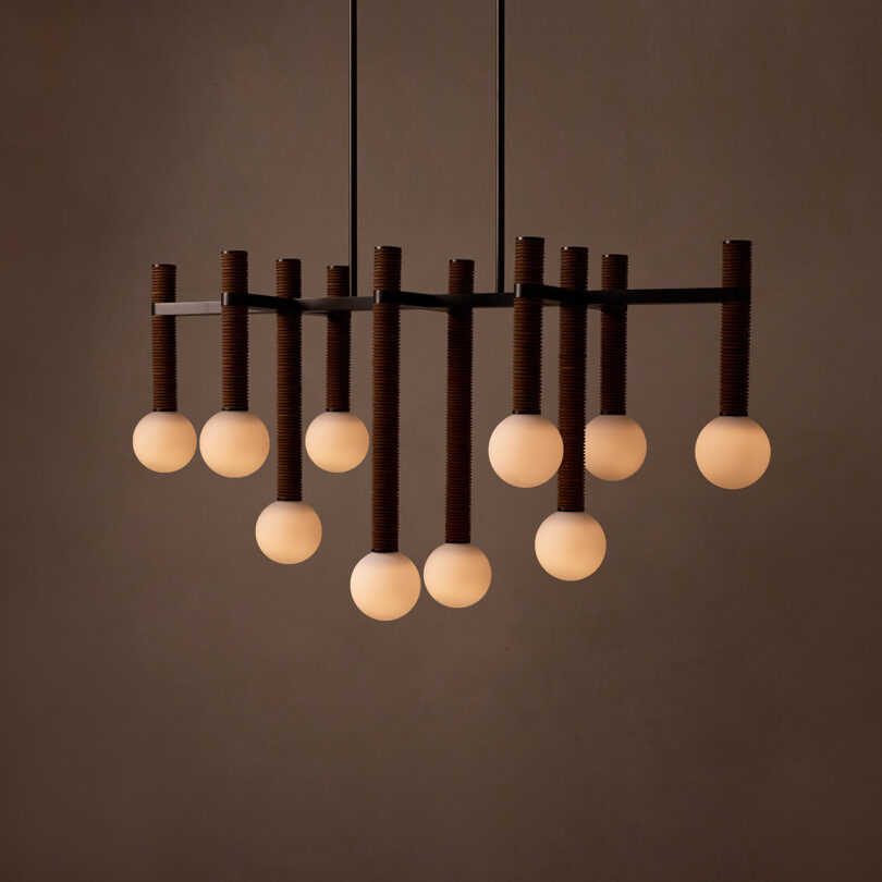 A modern Pell chandelier from Studio Luddite showcases a geometric design with 12 spherical light bulbs arranged in a staggered pattern against a dark background.