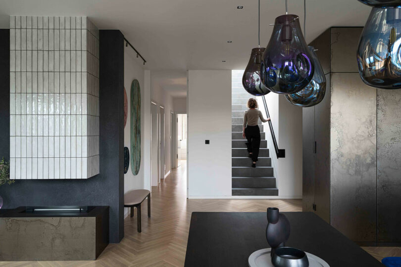 A person ascends a staircase in a modern, minimalist home interior with stylish lighting and decor.