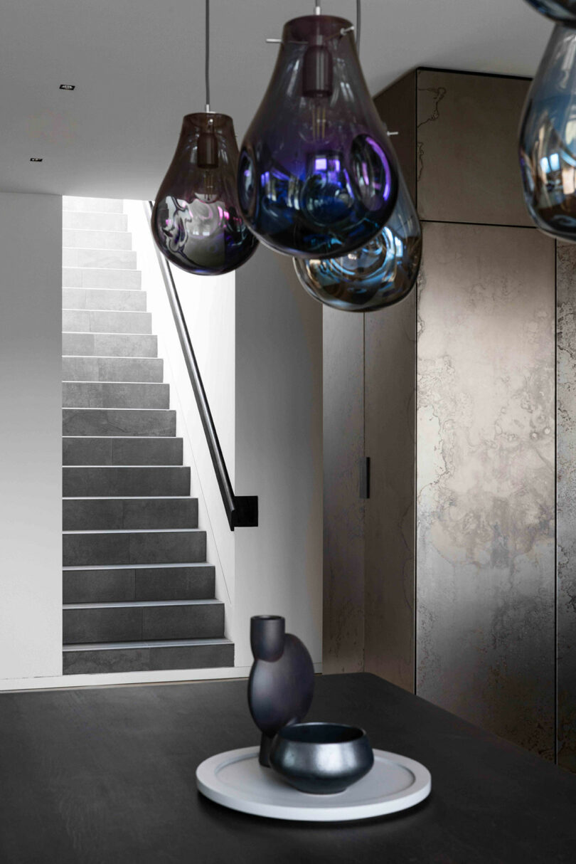 Modern interior with a staircase, dark decorative table items, and hanging glass pendant lights.