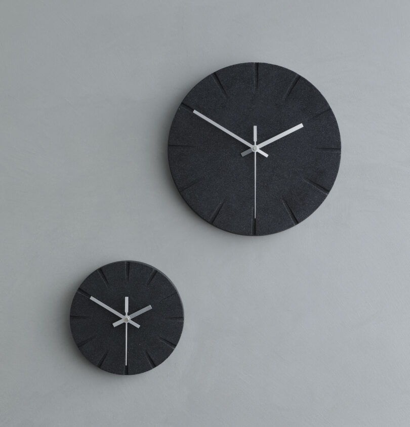 Two modern black wall clocks of different sizes with minimalist design on a gray wall