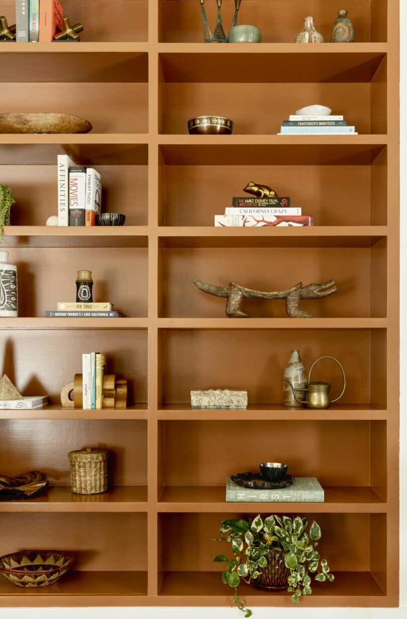 A wooden bookshelf with decorative items, books, pottery, and plants arranged on the shelves.