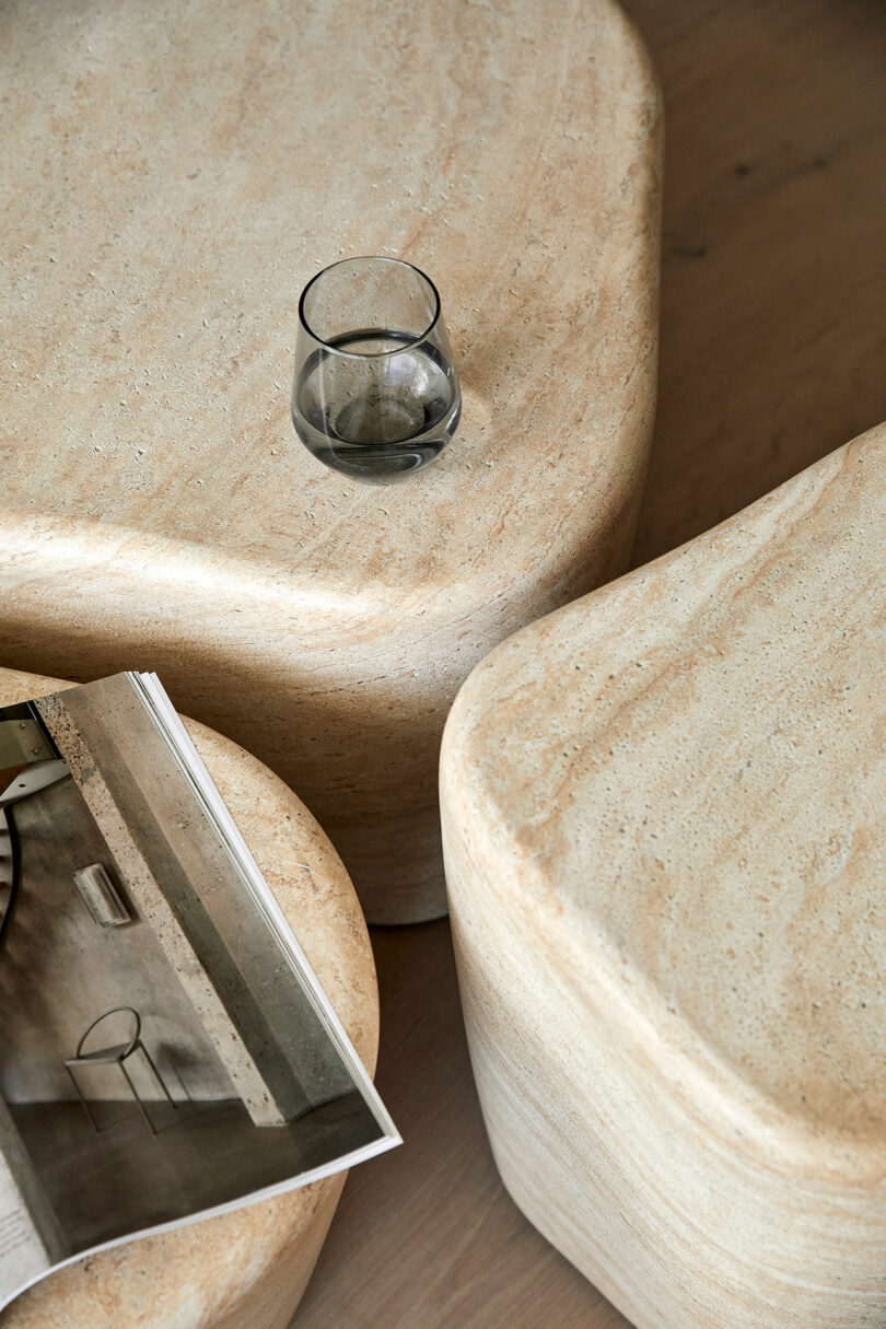 Stone tables with curved edges, one topped with a glass of water, and another with an open magazine displaying an interior design feature