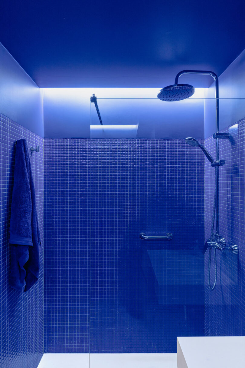 Une douche moderne avec du carrelage bleu, une pomme de douche à effet pluie et une serviette accrochée à un crochet.