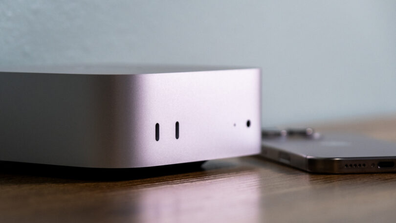 A silver desktop computer on a wooden surface, next to a smartphone.