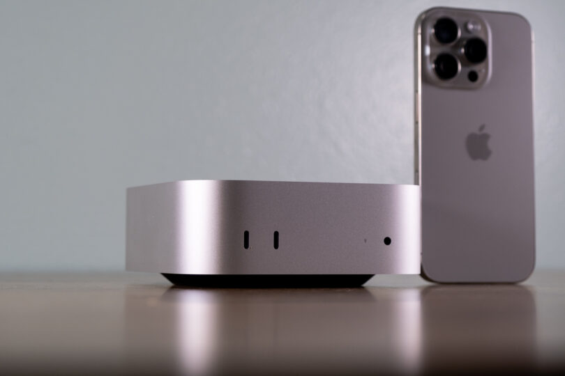 A compact silver device sits on a table next to a smartphone.