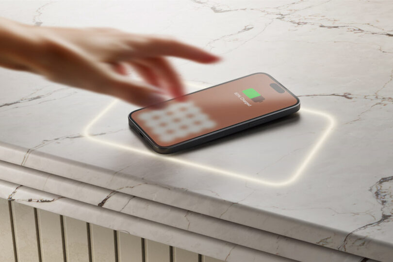 A hand reaches for a smartphone charging on a marble countertop with a glowing outline.