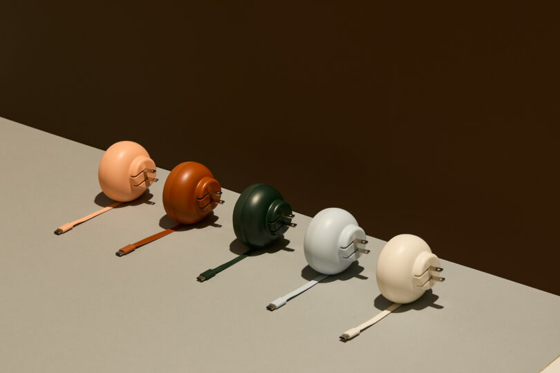 Five spherical chargers in pastel shades are aligned diagonally on a two-toned surface. Each charger has a matching USB cable attached.