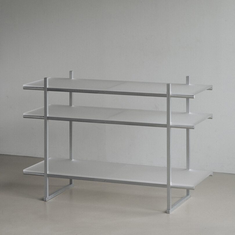 A three-tiered, minimalist white shelving unit against a plain wall on a light floor.