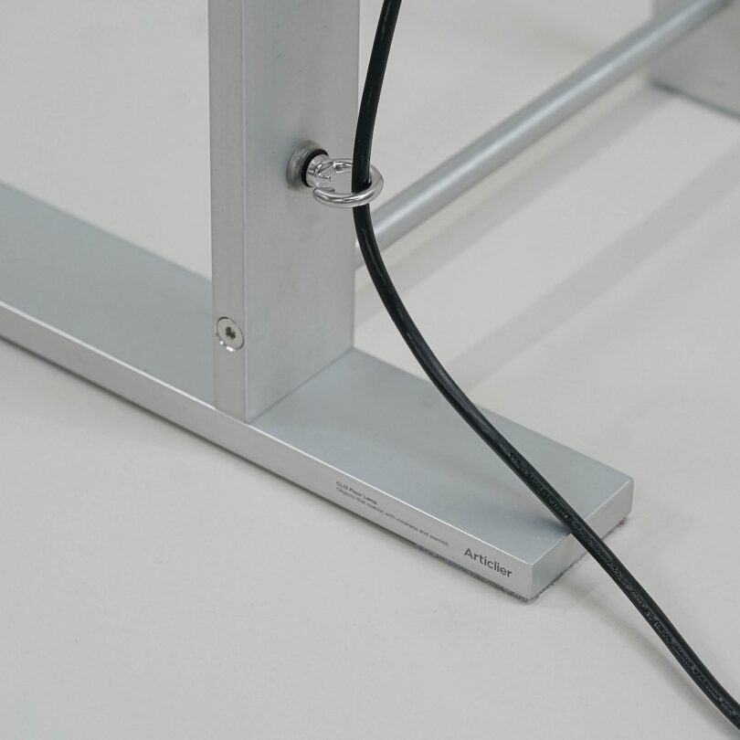 Close-up of a metal frame with a black cord looped through a ring on the frame. The base features text, including the word "Artcifer." The setup is on a smooth, pale surface.