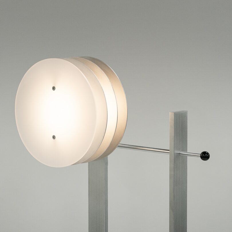 A modern table lamp with three circular shades on a metallic stand, featuring a horizontal rod and minimalistic design.