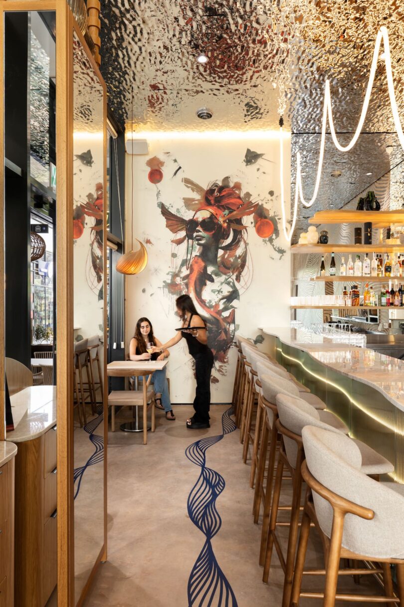 Two people converse at a table in a modern bar with a sleek counter and abstract wall art