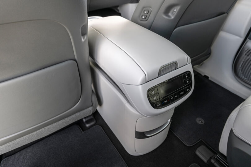 Rear car interior showing a modern white center console with a digital control panel, surrounded by grey seat backs and black carpeting.