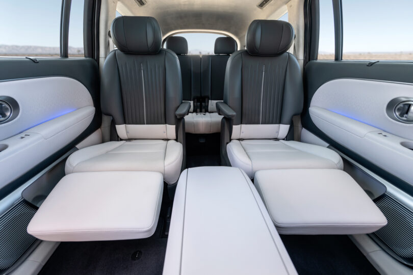 The interior of a spacious car features four individual leather seats with footrests and a minimalist design, including built-in armrests and ambient lighting.