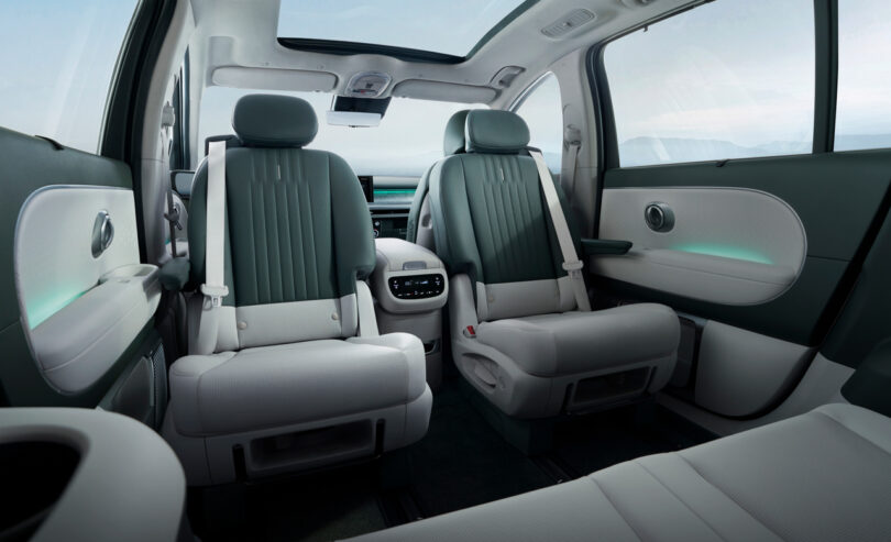 Interior of a modern car with two rows of leather seats. The front seats are turned to face the back, and an overhead skylight is visible. The dashboard is equipped with a digital screen.