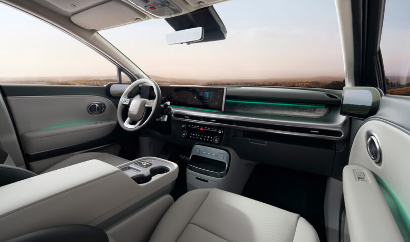 Interior of a modern car displaying a sleek dashboard, large touchscreen, and two-tone seats. The steering wheel and console are visible, with ambient lighting and a panoramic view through the windows.