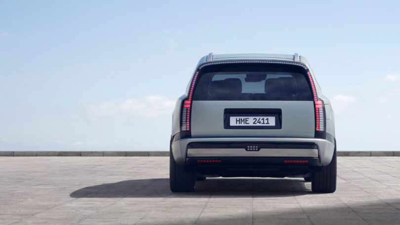 A silver SUV is parked on a stone pavement, viewed from the rear with a clear sky in the background.