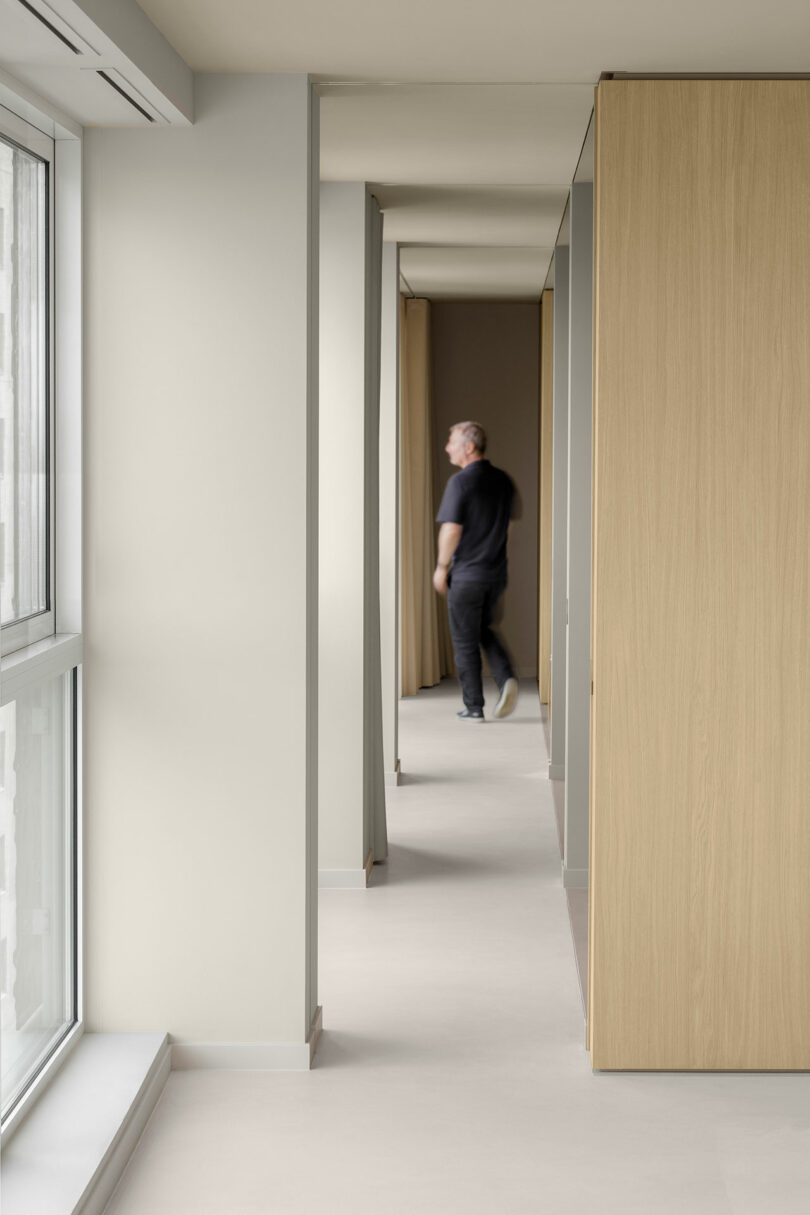 A person walks down a bright, modern hallway featuring light wood paneling and large windows.