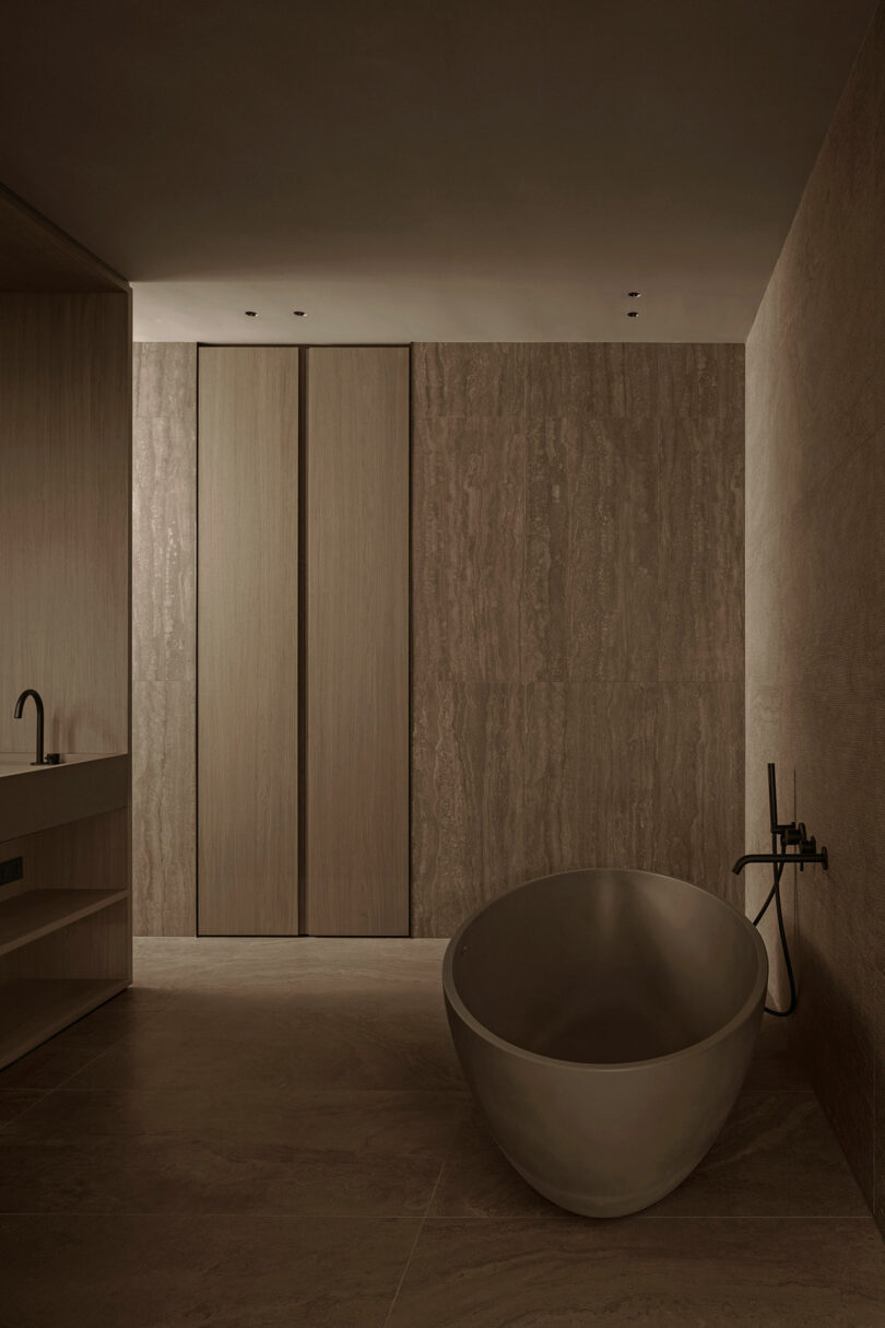 Minimalist bathroom with a large freestanding oval bathtub, wall-mounted faucet, and wood-paneled walls in neutral tones.