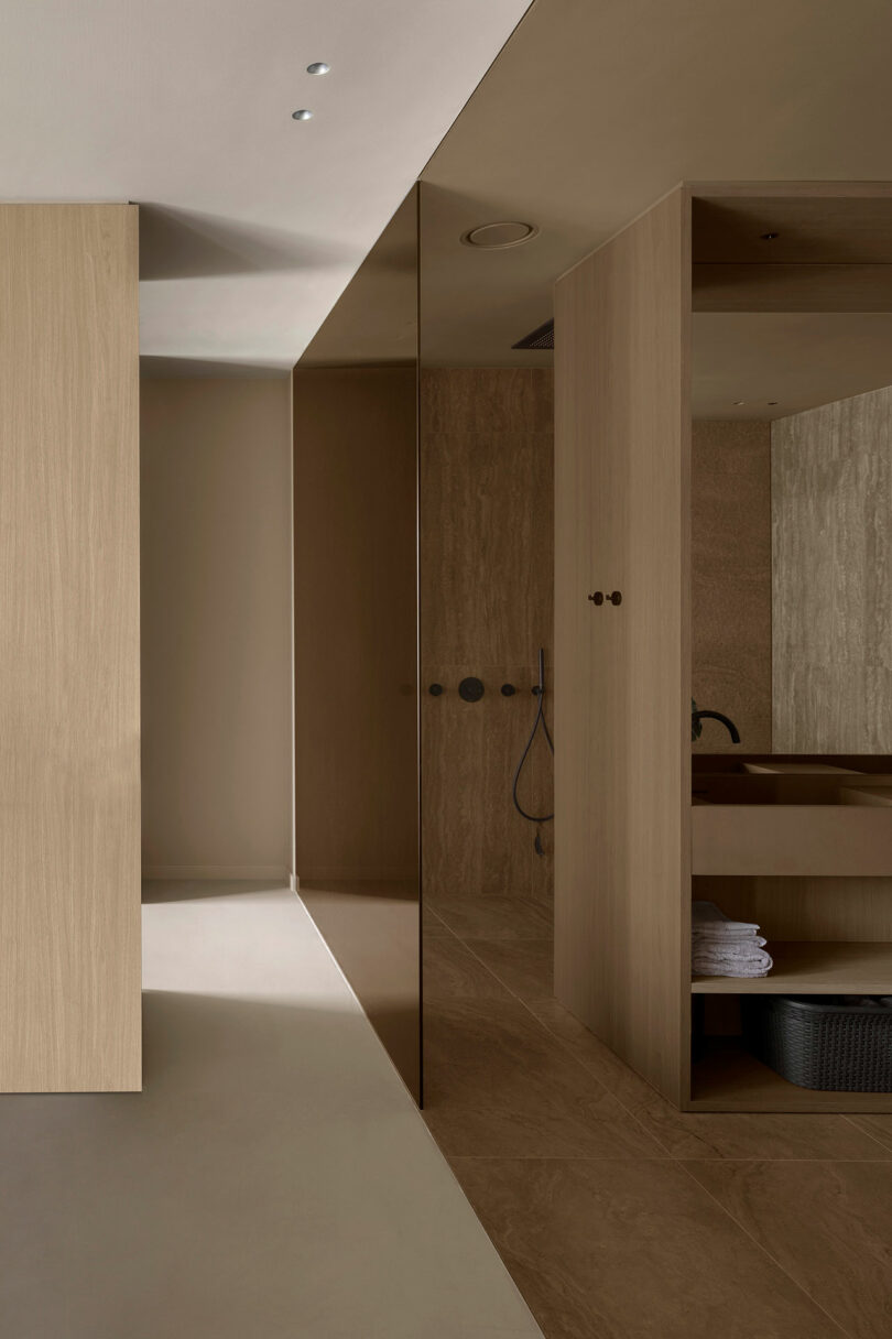 Baño minimalista con gabinetes de madera, puerta con espejo y una moderna zona de ducha. La iluminación suave resalta el diseño limpio y simple.