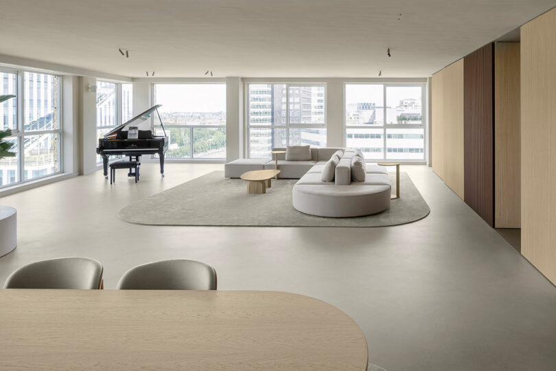 Spacious modern living room with large windows, a grand piano, minimalist furniture, and a neutral color palette.