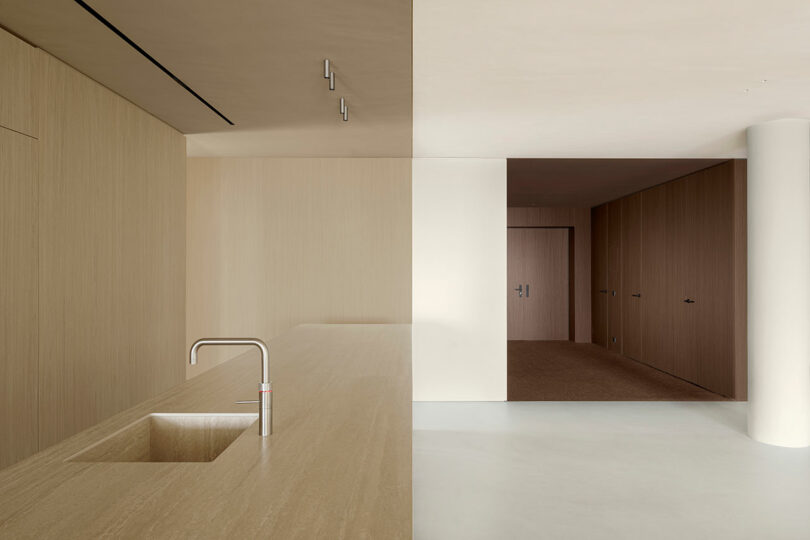 Minimalist interior with a beige color scheme, featuring a wooden countertop and sink on the left, smooth walls, and a hallway leading to a door.