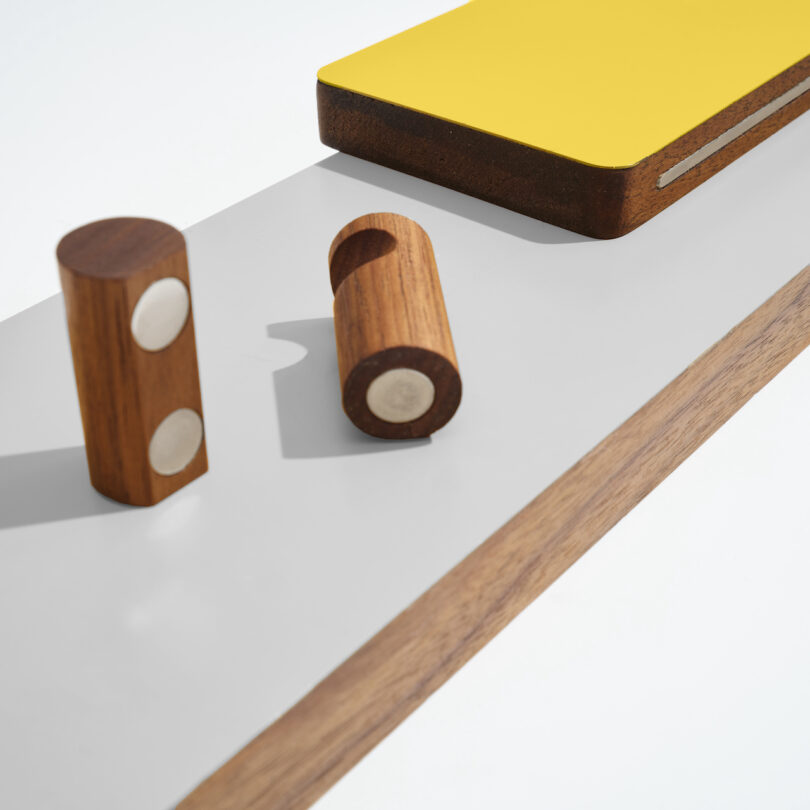 Wooden cylindrical pieces with metallic ends and a book with a yellow cover on a gray and wood surface