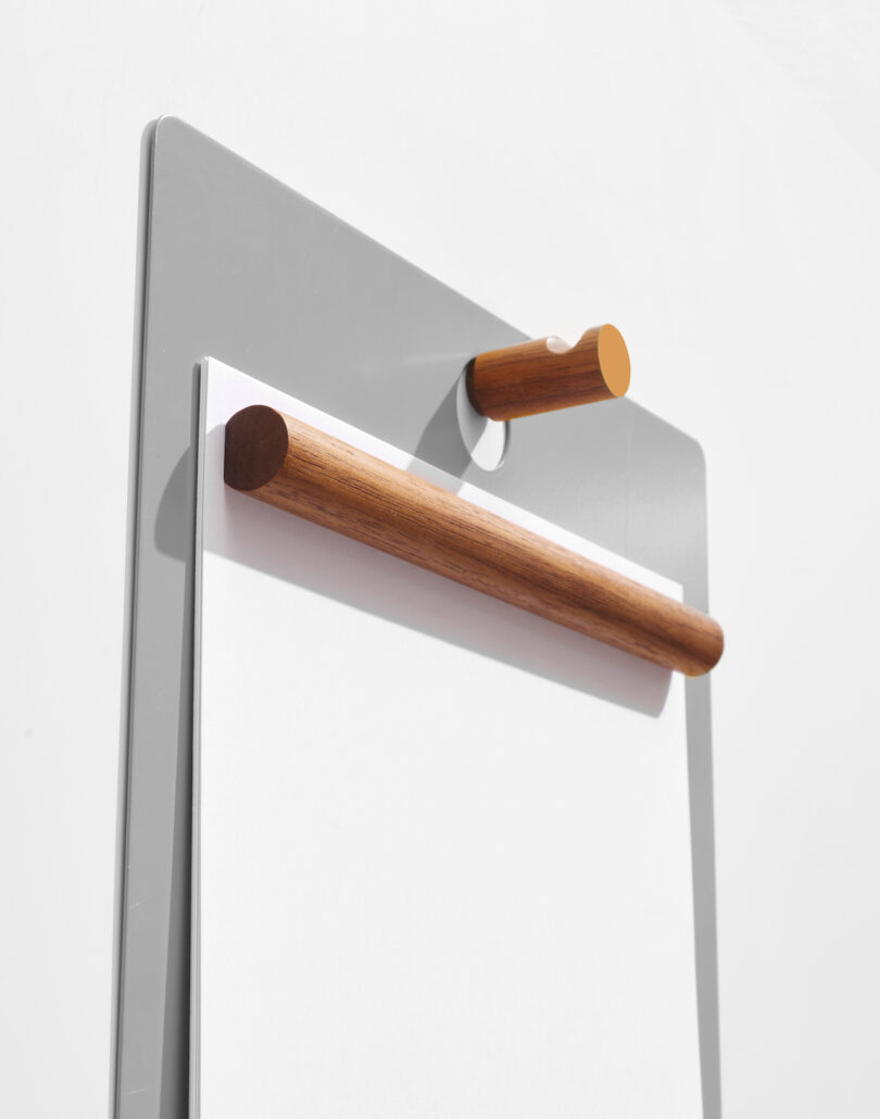 Side view of a clipboard with a wooden clip holding sheets of paper, attached to a wall