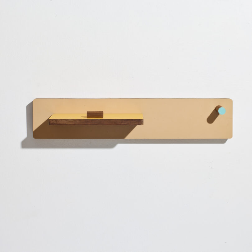 Minimalist wall-mounted shelf with a wooden plank and a small round peg on a beige background