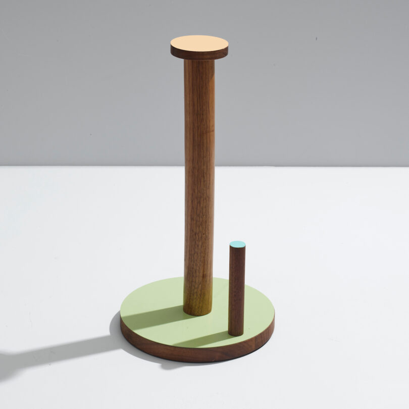 A minimalist wooden sculpture with two vertical cylinders on a circular base, featuring pastel colors