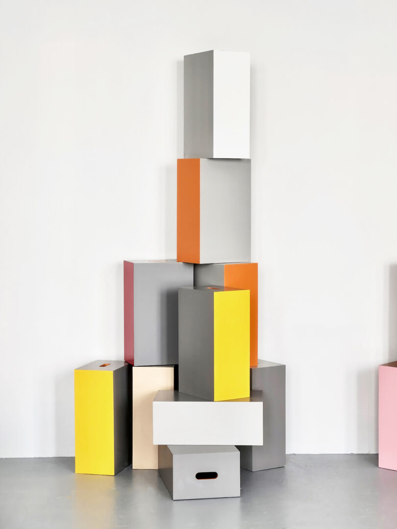 Stack of colorful rectangular boxes against a plain white wall, including gray, yellow, orange, and pink