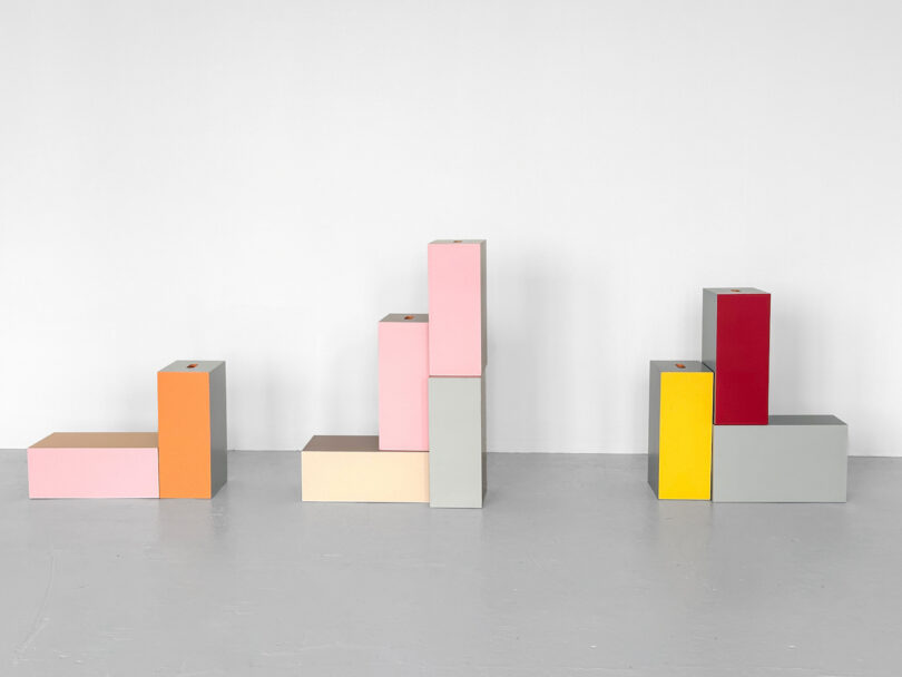 Colorful geometric blocks stacked in three separate groups against a white wall