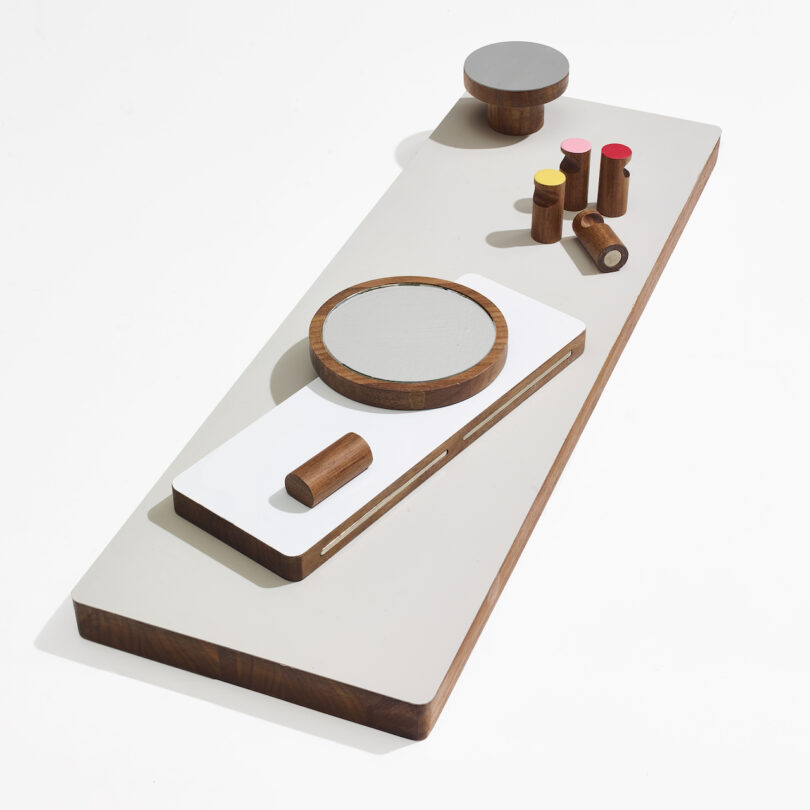 Geometric wooden objects on a rectangular board, including cylinders, discs, and blocks, arranged in a minimalist abstract design