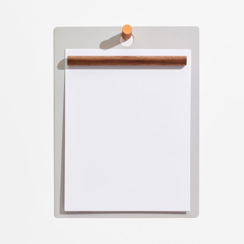 A clipboard with a wooden top handle holds a stack of white paper on a white background