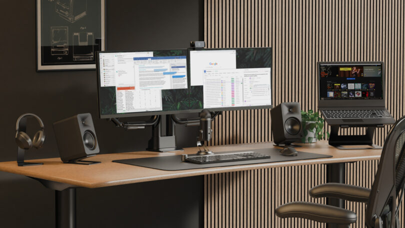 Modern office setup with dual monitors, a laptop on a stand, speakers, a keyboard, and headphones on a wooden desk with a black office chair.